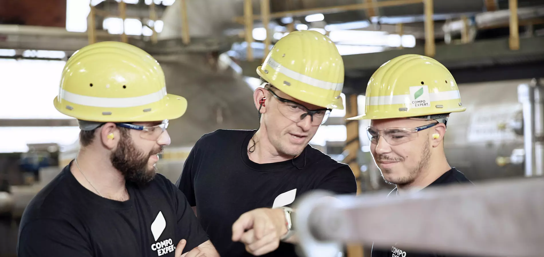 three men standing in a factory hall pointing at a device